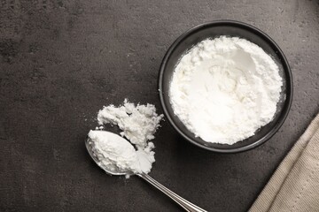 Baking powder in bowl and spoon on grey textured table, flat lay