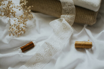 white patterned fabric ribbon and brown threads with needles against a background of delicate colors