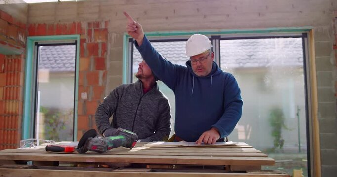 Construction workers using grinder tool on wooden table in building site, teamwork and collaboration, safety helmets, focused discussion on renovation project, indoors