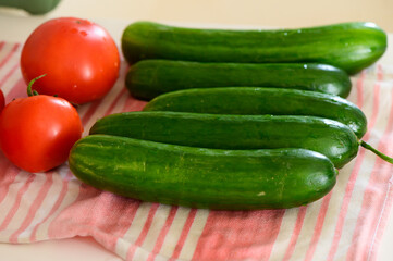 Fresh cucumbers and ripe tomatoes arranged on a striped kitchen towel in morning light
