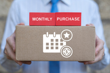 Business man holding cardboard box with calendar, money, star icon and red blocks with inscription: MONTHLY PURCHASE. Monthly Purchase Business Finance concept.