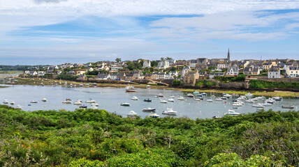 A scenic view of a coastal town of Conquet, Brittany, with numerous boats anchored in a calm bay, surrounded by lush greenery.