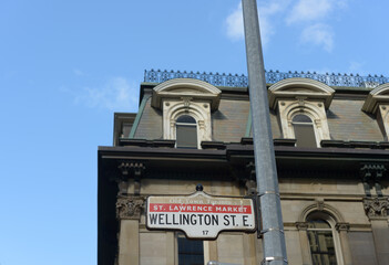 Fototapeta premium vintage Old Town Toronto, St Lawrence Market road sign for Wellington Street East (at Yonge St) with historic building and sky behind