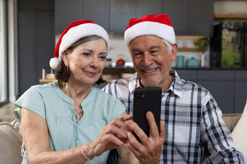 Christmas time, senior couple wearing santa hats using smartphone, at home