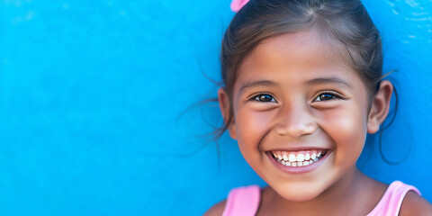 Portrait of little latina girl smiling, wearing pink t-shirt, blue background