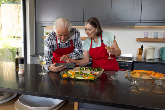 Senior couple cooking together in kitchen, using tablet for recipe guidance, at home