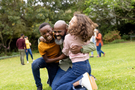 mutliracial family enjoying playful hug outdoors, laughing together in sunny park
