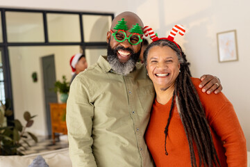 Happy multiracial couple wearing festive accessories, smiling together at home during Christmas