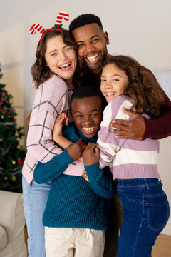 Happy multiracial family hugging by Christmas tree, celebrating holiday together at home
