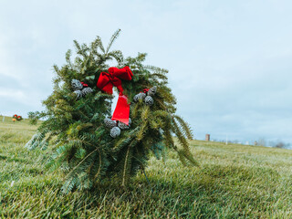 Christmas holiday festive wreath decorated with pine cones and a red bow at grassy cemetery 