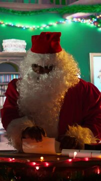 Vertical Video African american Father Christmas decorates boxes of presents with ribbons in his North Pole log workshop, delivering the gifts on x mas eve. Festive season with holiday magic. Camera B