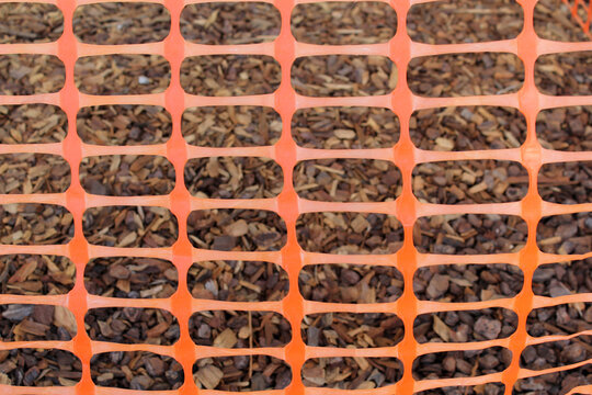 Close-up of an orange plastic mesh fence barrier surrounding wood chip in a garden