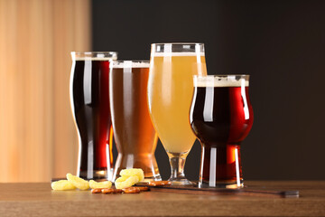 Glasses with different types of beer and snacks on wooden table indoors