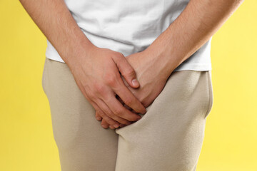 STD (sexually transmitted diseases). Man suffering from symptoms on yellow background, closeup