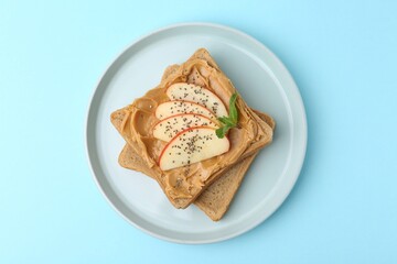 Tasty sandwich with peanut butter, apple, chia seeds and mint on light blue background, top view