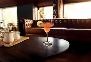 A refreshing cocktail with a salted rim sits on a coffee table in a dimly lit room with leather furniture.