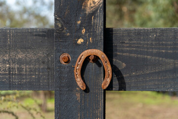 A rustic horseshoe hanging at the entrance of a corral, symbolizing good luck and tradition. The worn metal against the wood backdrop creates a timeless rural charm.