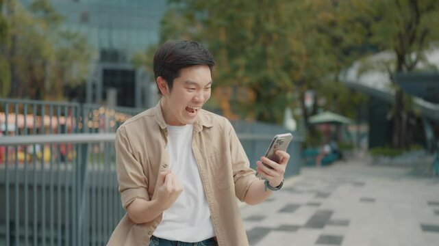 Young Asian handsome man watching mobile smartphone and wearing casual very happy and excited doing winner gesture with arms raised, smiling and screaming for success