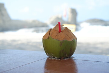 A freshly opened green coconut with a red straw sits on a table