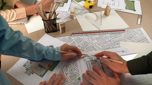 Smart architect and safety engineer discussion about building blueprint on table with architectural document, measurement tools and wooden block scatter around at modern office. Closeup. Delineation.