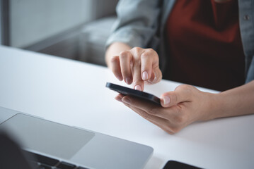 Woman using mobile phone with laptop computer on office table. Business woman surfing the internet, searching the information on smartphone working on laptop computer at workplace