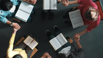 Top down view of diverse people holding hand and sitting in circle with bible book on lap. Aerial view of faithful prayer clasp hand and praying to god with faith, religion conceptional. Symposium.