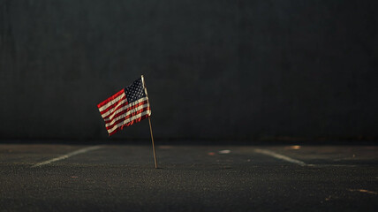 A small American flag stands alone in an empty parking lot during early morning light