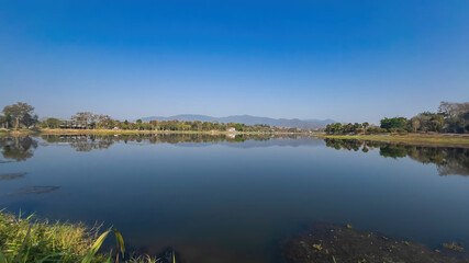 A panoramic view of Nong Bua Lake in Chiang Rai, Thailand, showcasing its serene waters surrounded by lush greenery and distant mountains. 