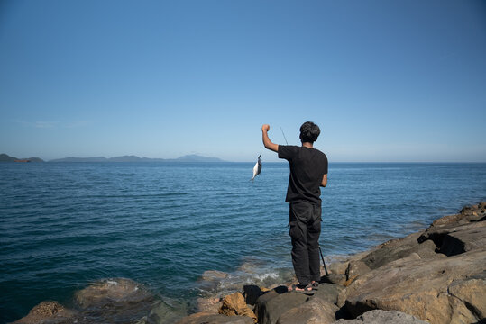 A man fishing on a rocky shore in sunny weather - Powered by Adobe