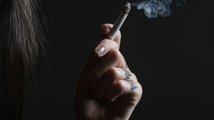 Fototapeta premium Fierce Choice: Woman's Tattooed Arm with Cigarette in Close-Up, Symbolic of Life Decisions in Dark Background