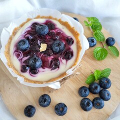 Molten Blueberry Cheese Tart, topped with blueberry filling and fresh blueberries, on a round wooden chopping board