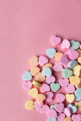 flat lay of a pile of pastel colored candy hearts in blue, green, pink, yellow, and orange against a pink background with copy space available, valentine's day themed