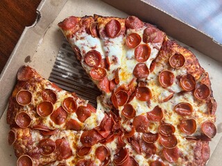 Slice missing from a large pepperoni pizza with cheese in a cardboard box. Takeout delivery to-go from a restaurant.