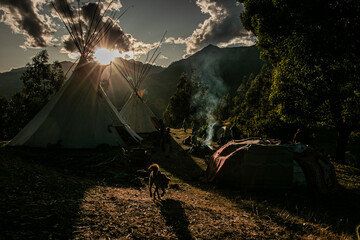 Native community with people in a landscape with teepee and temazcal in a sunrise with the sun rising over the mountains. 