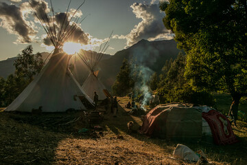 Native community with people in a landscape with teepee and temazcal in a sunrise with the sun rising over the mountains. 