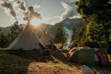 Native community with people in a landscape with teepee and temazcal in a sunrise with the sun rising over the mountains. 