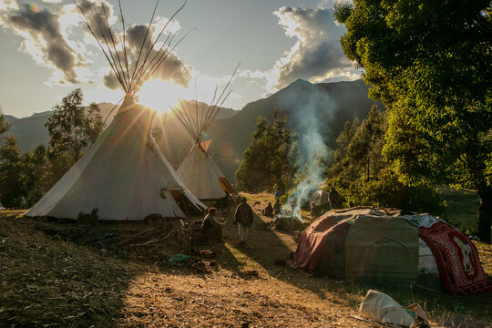 Native community with people in a landscape with teepee and temazcal in a sunrise with the sun rising over the mountains. 