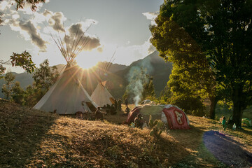 Native community with people in a landscape with teepee and temazcal in a sunrise with the sun rising over the mountains. 