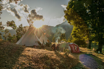 Native community with people in a landscape with teepee and temazcal in a sunrise with the sun rising over the mountains. 