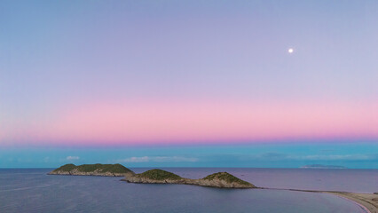 The full moon shines over the islands off the beach in San Carlos Sonora, Mexico. The light of dawn...