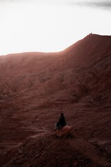 Vertical shot of a Hispanic man sitting on a rock at San Pedro de Atacama desert at sunset, Chile