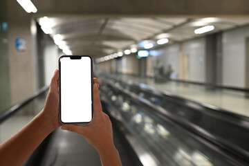 Hands holding smartphone with blank display on airport moving walkway