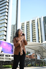Fototapeta premium Cheerful mature businesswoman enjoying a phone conversation in front of skyscrapers