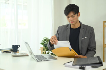 Concentrated businessman examining important documents at work desk