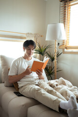 Handsome asian man in casual clothing relaxing at home with a book and coffee