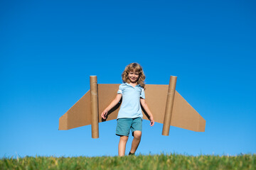 Naklejka premium Happy child playing with toy jetpack. Kid pilot having fun on green grass outdoor. Success, kids innovation and leader concept.