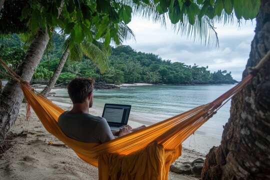 A man working on laptop computer while relaxing in beach hammock