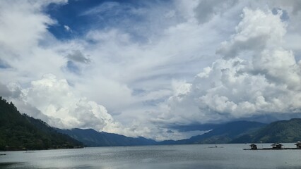 Obraz premium A serene lake surrounded by lush green hills under a cloudy sky.