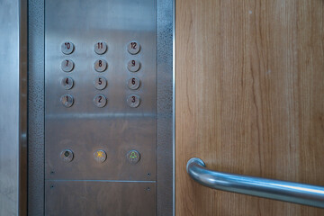 Round metallic buttons on an elevator control panel with wooden interior wall.