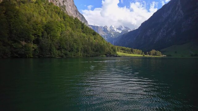 A beautiful landscape of Konigsee natural lake in Berchtesgaden Bavaria Germany in slow motion with river water in the foreground Bavarian Alps mountains clouds and Blue sky in the background.